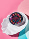 Round black pinback button with vibrant floral embroidery design surrounding bold pink and red text reading "Dissent is Patriotic."